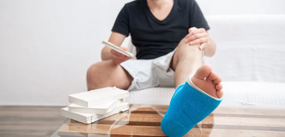 man-with-broken-leg-blue-splint-treatment-injuries-from-ankle-sprain-reading-books-home-rehabilitation