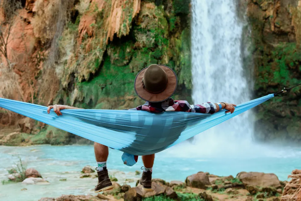 wide-shot-male-lying-hammock-beside-waterfall-flowing-down-from-hill