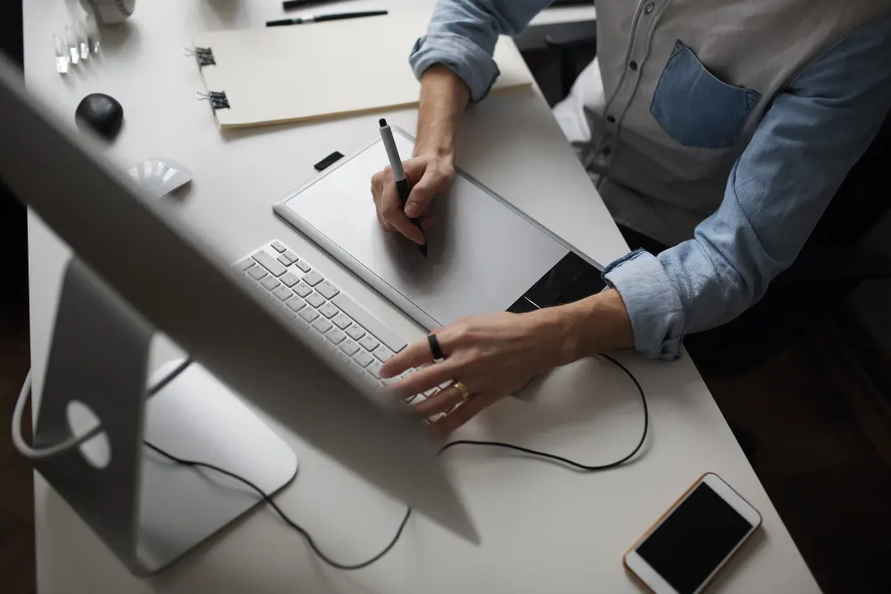 young-male-designer-using-graphics-tablet-while-working-with-com