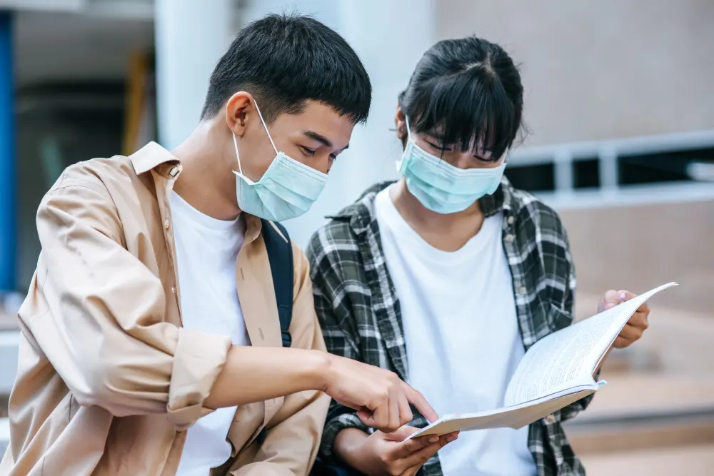 male-and-female-students-wearing-masks-sit and-read-books-on-the-stairs