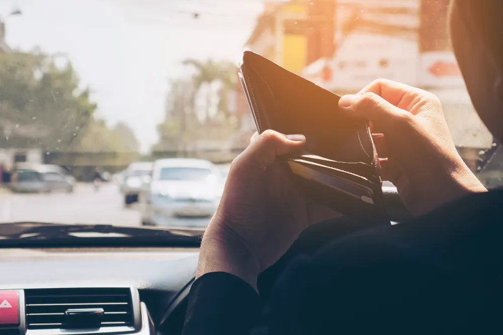 man-look-at-his-empty-wallet-while-driving-car