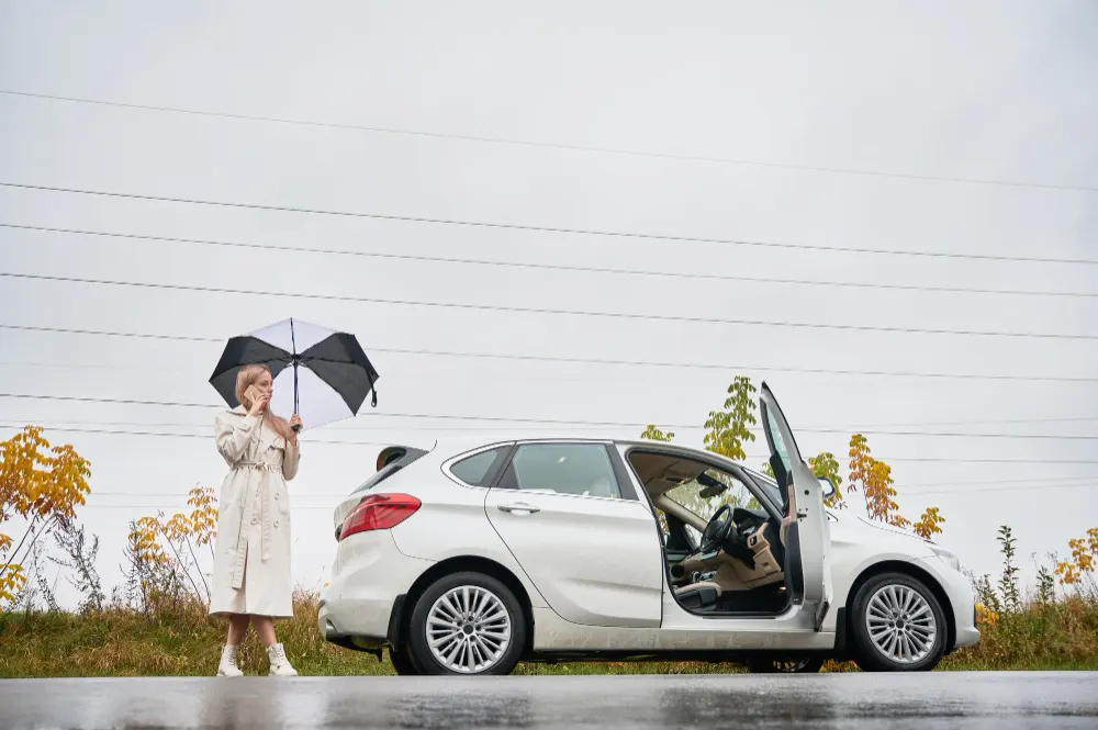 woman-with-umbrella-standing-near-car-and-speaking-on-phone