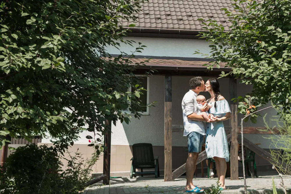 Couple-carrying-their-baby-kissing-in-front-of-home